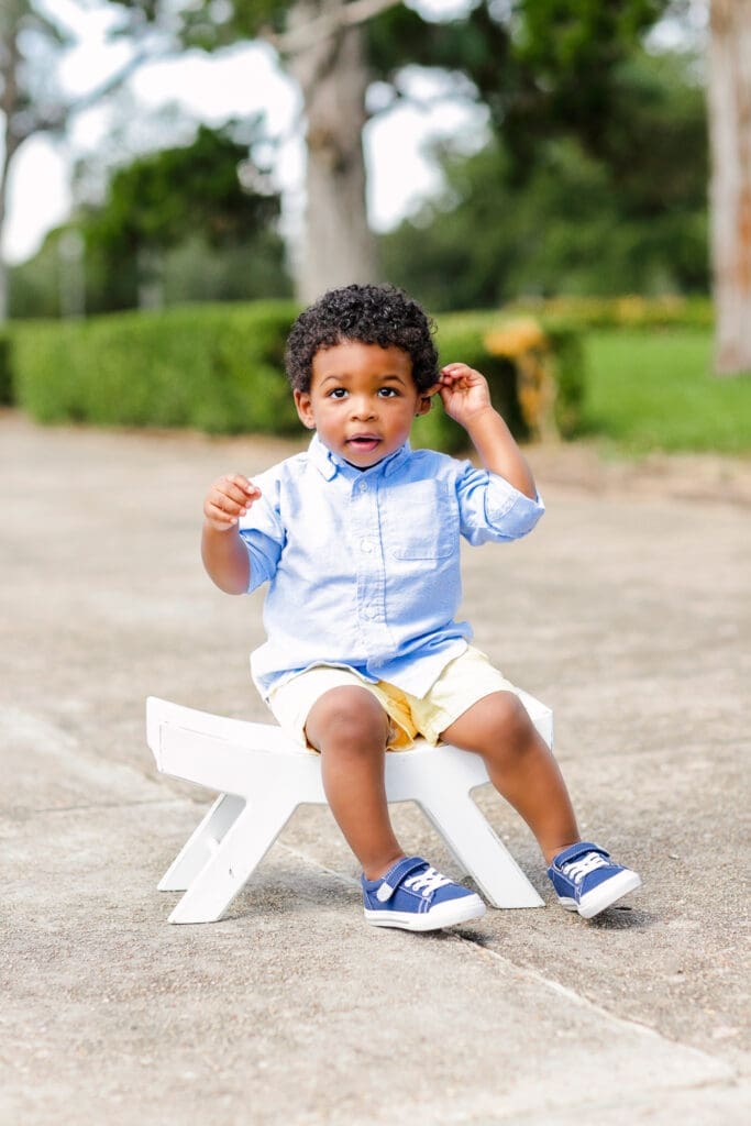 a little boy sitting on a white chair smiling at the camera in baton rouge