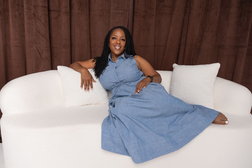 Woman wearing a blue dress seated on a white sofa during a lifestyle branding session.